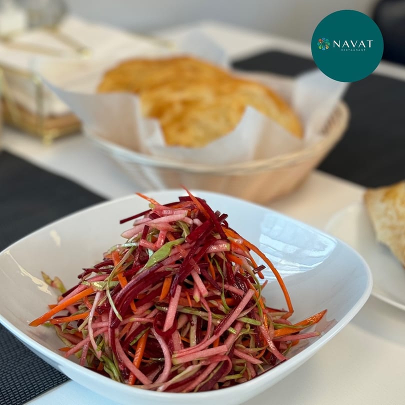 A white bowl filled with a colorful Russian salad of shredded beets, carrots, and cabbage.