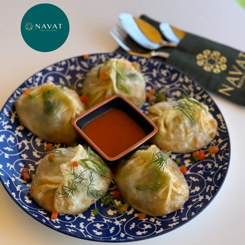 Five golden-fried Russian dumplings (manti) with herbs and diced vegetables, served with red sauce on a blue plate.
