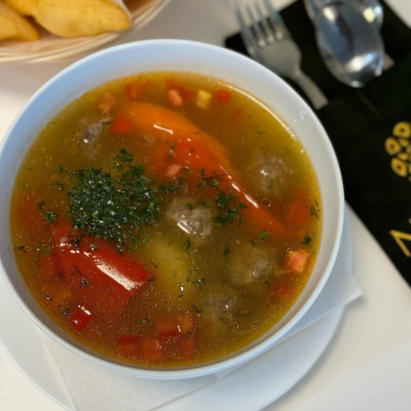 A bowl of Russian soup with meatballs, red bell peppers, and dill, served with bread.