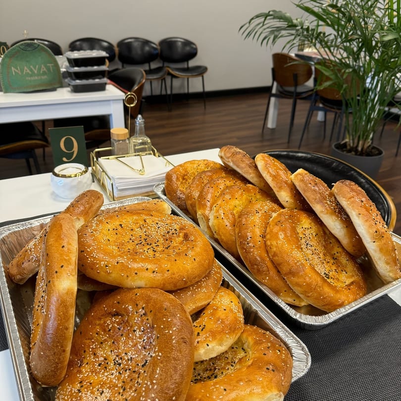 Trays of freshly baked Russian bread, some round and some elongated, topped with sesame seeds.